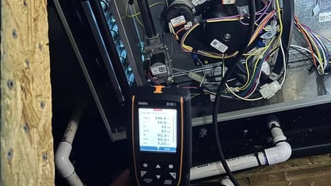 Gas furnace opened up with the control board and wiring exposed while a digital combustion analyzer reads the system